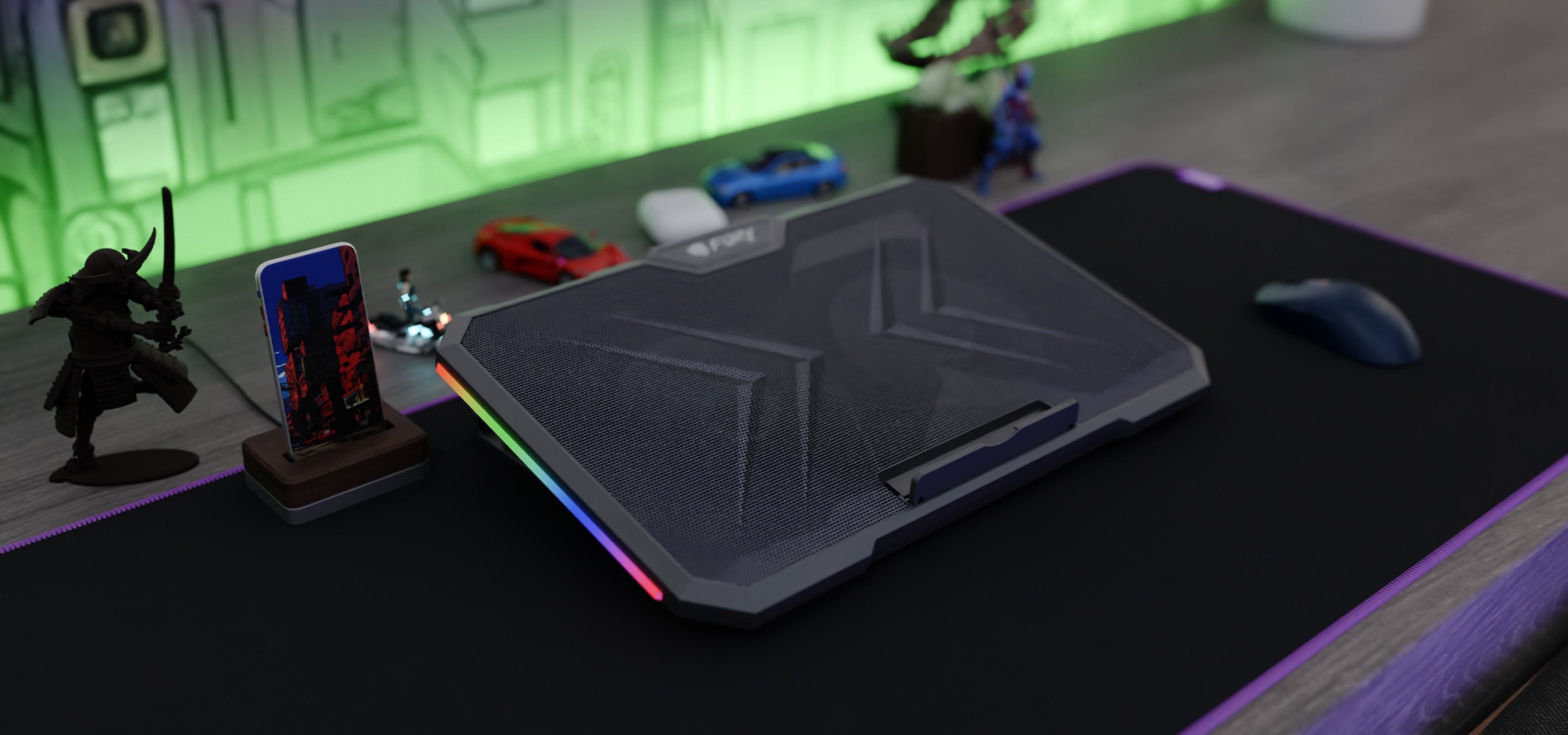 Laptop cooling pad with RGB lighting on a desk with a mouse and small decorative figures.