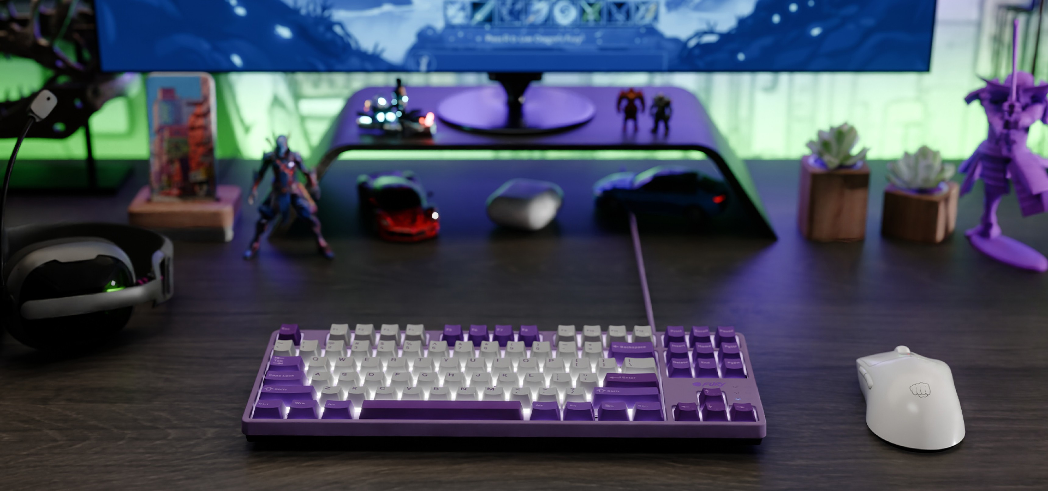 A purple keyboard and a white mouse on a desk with figurines and a computer monitor in the background.